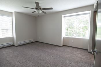 an empty room with a ceiling fan and two windows